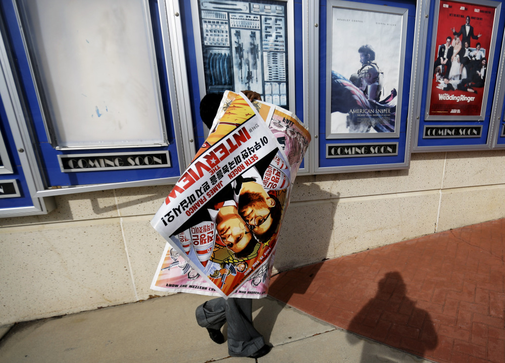 A worker carries away a poster for the movie “The Interview” after pulling it from a display case at a Carmike Cinemas movie theater in Atlanta on Wednesday.