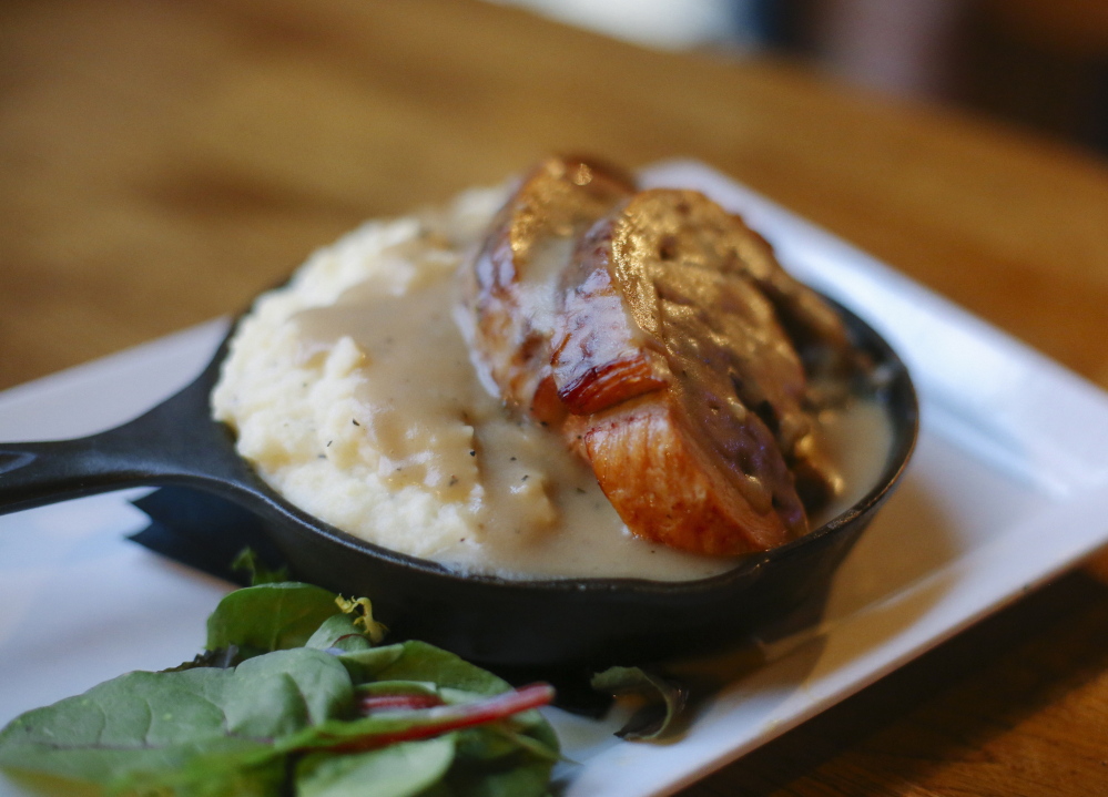 Stuffed pork loin is served with mashed potatoes and gravy in a cast iron skillet.