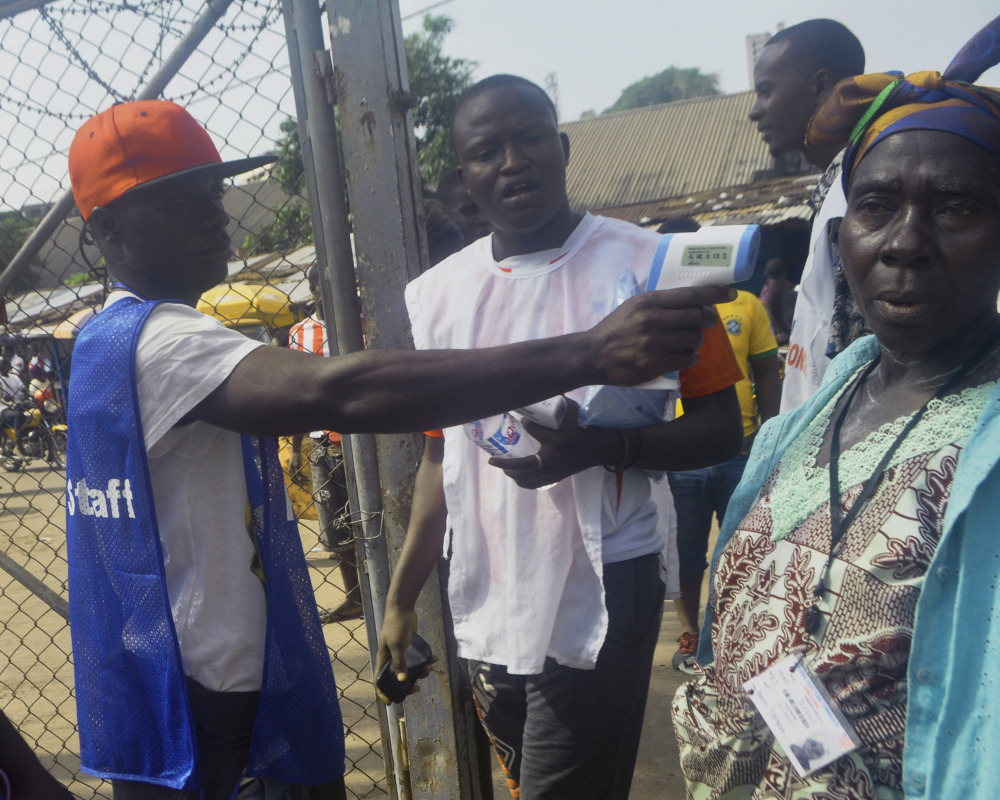 An election worker takes the temperature of a voter in the West Point slum before she casts her vote Saturday during a Liberian election.