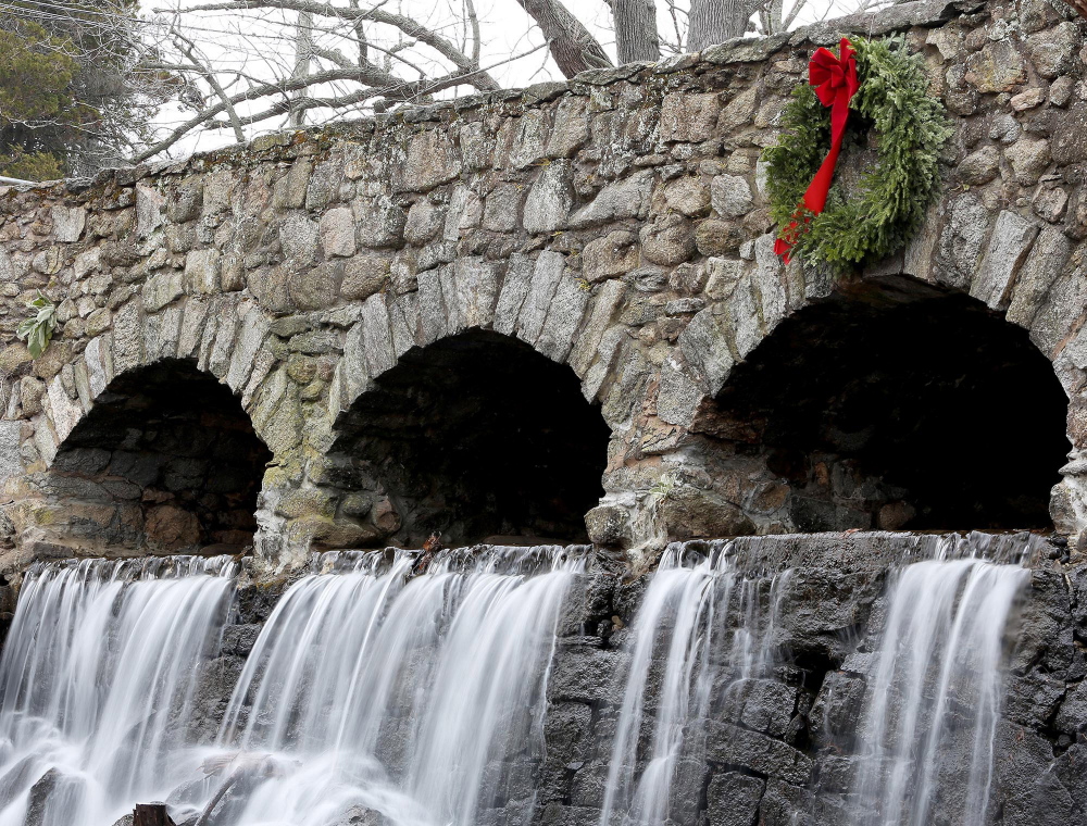 A wreath hangs above a waterfall at Case Pond in Manchester, Conn. It is a mystery who adds the wreath to the bridge every December, but the holiday flair is welcome.