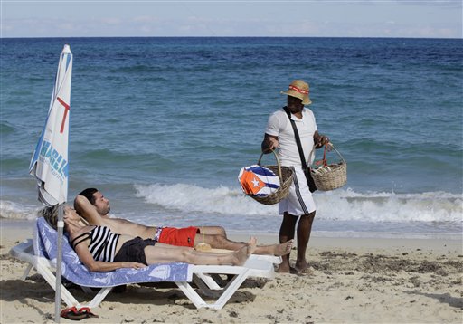Tourists sunbathe on a beach near Havana, Cuba, as a vendor sells kites decorated with Cuba's flag. The Associated Press