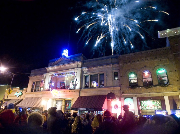 In this Dec. 31, 2013 photo, the crowd cheers and fireworks explode in the sky as a lighted cowboy boot drops to the roof of the Palace Saloon New Year's Eve on Whiskey Row in downtown Prescott, Ariz.