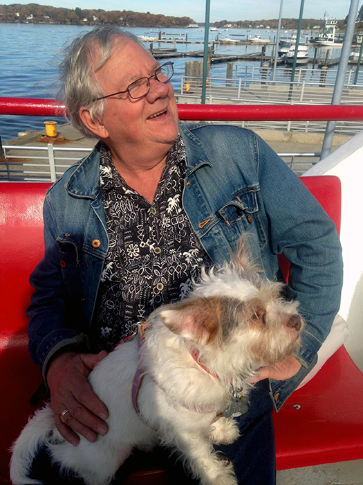 In this undated photo provided by Caren Ferris, John Ferris rides with his adopted dog Ginger on a ferry to Peaks Island, Maine. Ferris, from Amherst, Mass., with his wife, adopted Ginger from the Aloft Hotel in downtown Asheville, N.C., where the couple were staying nearby when they met the 4-year-old terrier mix in the hotel bar sporting an "Adopt Me" vest. The Associated Press