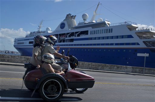 A trio of people ride a motorcycle with sidecar past the Semester at Sea cruise ship docked in Havana's harbor In this Dec. 9, 2013, photo. The Associated Press