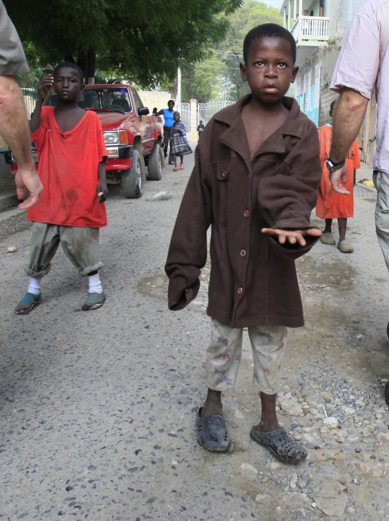 A boy asks for money as foreign visitors walk past him on a street in Cap Haitien, Haiti.