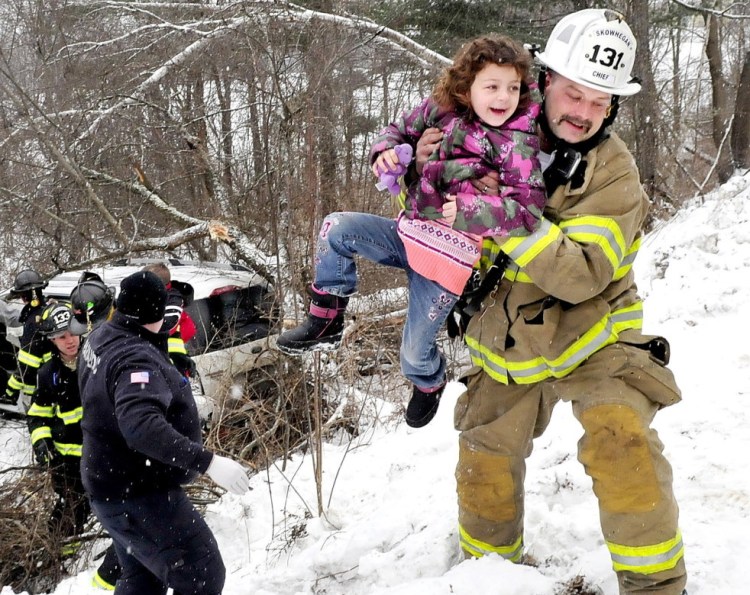 Skowhegan Fire Chief Shawn Howard carries a young girl from a vehicle that slid off Norridgewock Road in Skowhegan, went down a ravine and struck a tree Monday. Four children and the driver escaped serious injury.