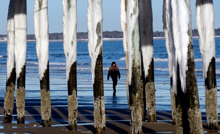 The pier's pillars in Old Orchard Beach are covered in snow and ice as Elisa Jacobs of Needham, Massachusetts, walks along the beach Thursday, two days after a blizzard and one day before Maine's next snowstorm.