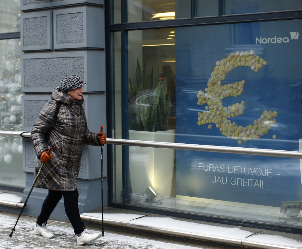 A woman walks by a poster reading “The euro is coming to Lithuania soon” in Vilnius, Lithuania, on Monday. Political leaders are hoping that joining the euro will help Lithuania distance itself further from Russian influence as well as boost the economy.