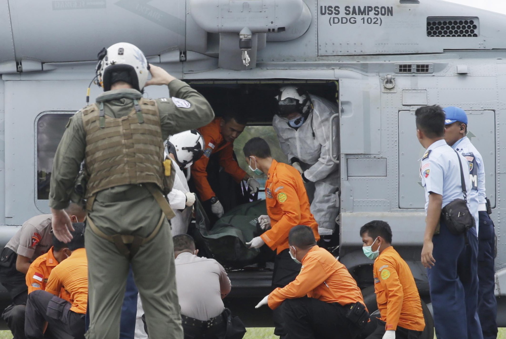 A U.S. Navy helicopter crew member salutes as the U.S. Navy personnel from USS Sampson unload the body of a victim from AirAsia Flight 8501 from the helicopter, assisted by Indonesian National Search and Rescue Agency personnel and policemen, upon arrival at the airport in Pangkalan Bun, Indonesia, on Friday. The Associated Press