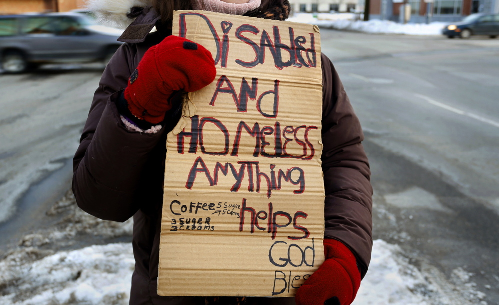 A panhandler holds a sign on the corner of Preble Street and Marginal Way in Portland. A city ordinance that bans people from standing on medians will be heard by a federal appeals court in Boston on Friday.