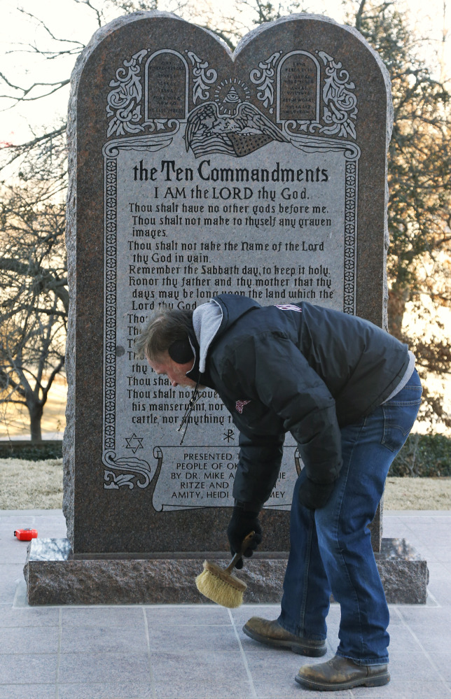Mike Sanford, who placed the foundation for the Ten Commandments monument, sweeps in front of the replacement after it was installed at the state Capitol in Oklahoma City on Thursday. Someone crashed a car into the original monument.