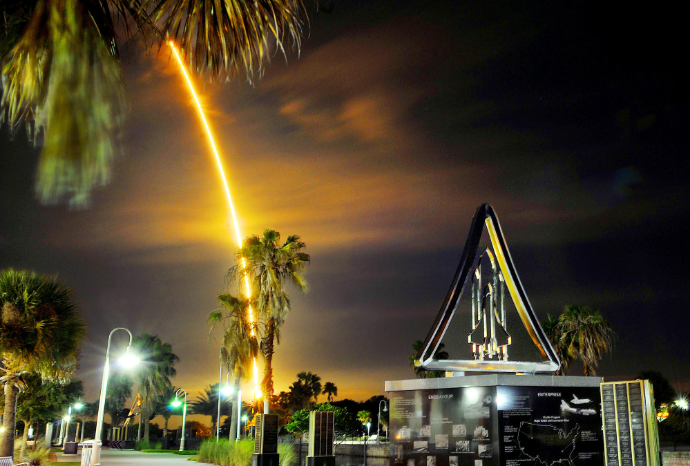 A SpaceX Falcon rocket with a Dragon cargo capsule aboard lights up the sky after liftoff from the Cape Canaveral Air Force Station launch complex as it streaks past a space shuttle monument in Titusville, Fla., early Saturday.