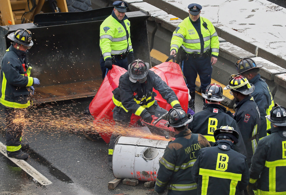 Firefighters use a saw to cut away a barrel that protesters locked themselves to in order to block the morning commute Thursday in Milton, Mass. Activists were protesting what they called “police and state violence against black people.”