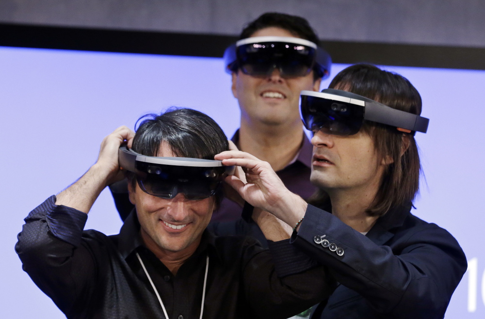 Microsoft’s Joe Belfiore, corporate vice president, left, tries on a “HoloLens” device with colleagues Alex Kipman, right, and Terry Myerson during a demonstration event at the company’s headquarters Wednesday.