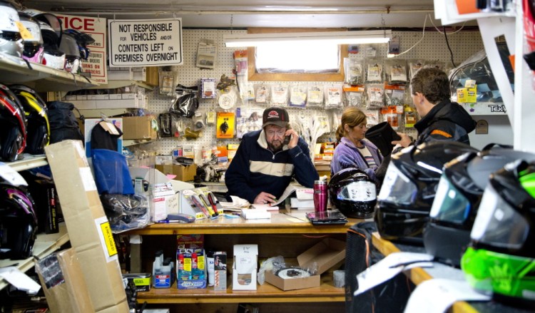 Wayne Keniston handles a call at his Falmouth store while shoppers anticipating good riding browse for snowmobile gear.