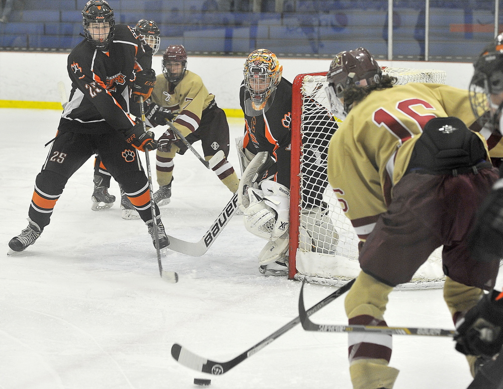 Tanner McFarren, right, of Thornton Academy looks for an opening to pass the puck to teammate Chandler Bilodeau, while Biddeford’s Mike Reissfelder, left, and goalie Brandon Daigle defend Saturday at Biddeford Ice Arena. Biddeford won, 4-0.