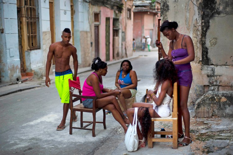 Hairdresser Lisandra works on a woman's extensions as others wait their turn in Old Havana, Cuba, on Tuesday. Lisandra attends her clients on the sidewalk outside her home. The Associated Press
