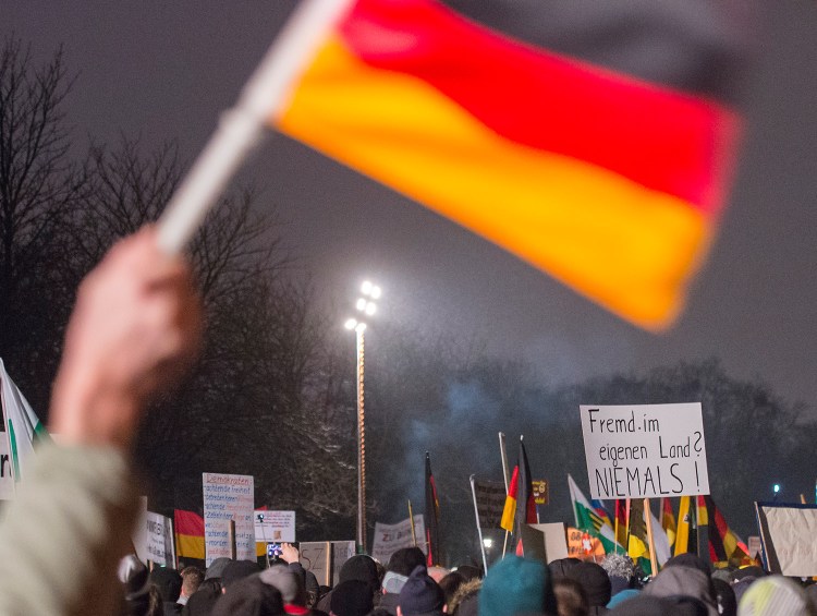 A participant of a rally by Patriotic Europeans against the Islamization of the West waves a German flag during a demonstration in Dresden, Germany, on Monday. The words on the banner, right, read: "Foreign in our own country? Never." Over the last three months, the crowds at PEGIDA's demonstrations in the eastern city of Dresden, a region that has few immigrants or Muslims, have swelled from a few hundred to 17,500 just before Christmas.