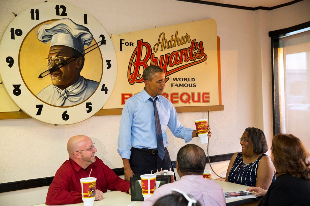 President Barack Obama picks up a souvenir cup while meeting with four Kansas City residents who wrote him letters, over dinner at a restaurant in Kansas City, Mo. Clockwise from left are Victor Fugate, the president, Becky Forrest, Valerie McCaw, and Mark Turner. Fugate is a guest to watch Obama's State of the Union address. The Associated Press