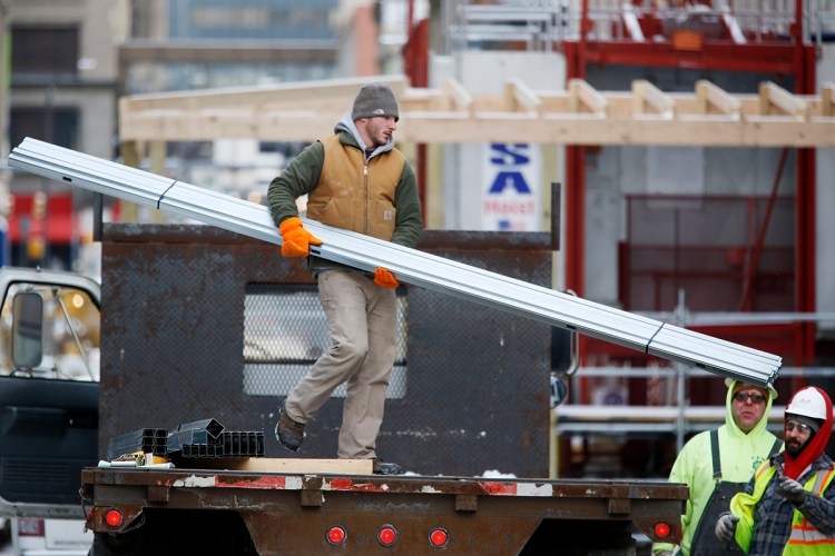 Workers unload construction materials at a building site in downtown Pittsburgh on Wednesday. Goldman Sachs estimates that low oil prices will lead to 300,000 more jobs in 2015 than would normally have been added if oil prices had stayed high. The Associated Press