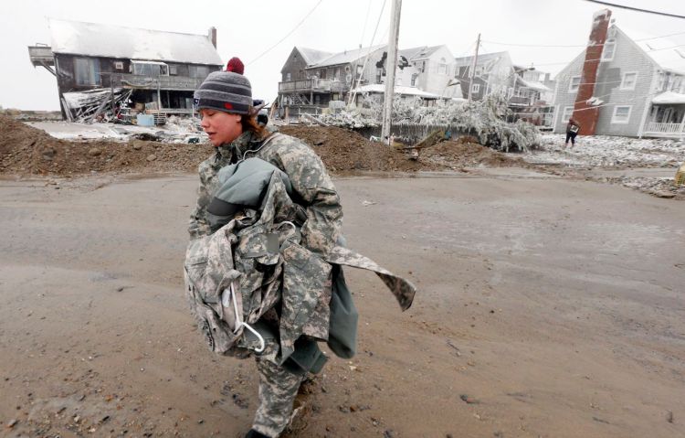 U.S. Army soldier Jennifer Bruno carries some belongings from her house, center rear, that was heavily damaged by a storm surge during the blizzard Tuesday in Marshfield, Mass. The Associated Press