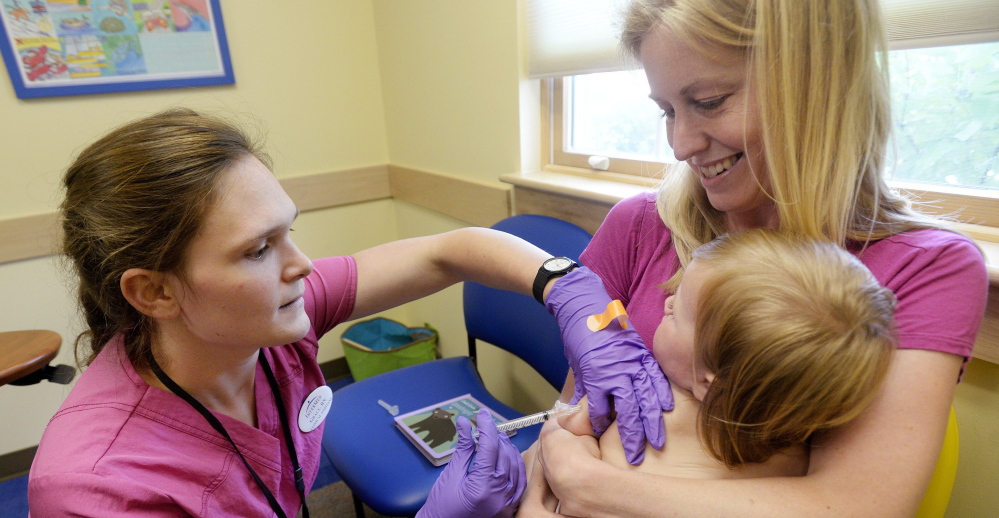 Amber Dugan holds daughter Tessa as she’s vaccinated in Yarmouth. The CDC calls for kids to get about 23 doses of 10 vaccines by age 2.