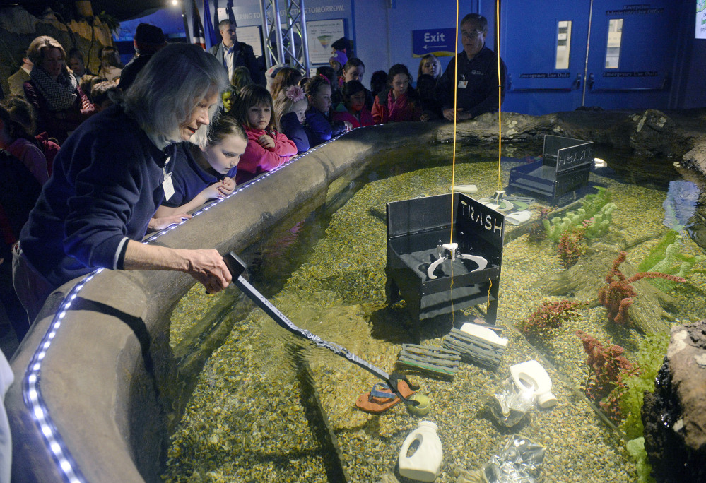 Patte Dunn of the Mystic Aquarium assists children as they operate a claw to pick up trash to deposit into a designated container as part of the new interactive Covanta Cove exhibit at the aquarium in Mystic, Conn. The exhibit is designed to educate visitors about how discarded marine debris can be turned into clean energy.