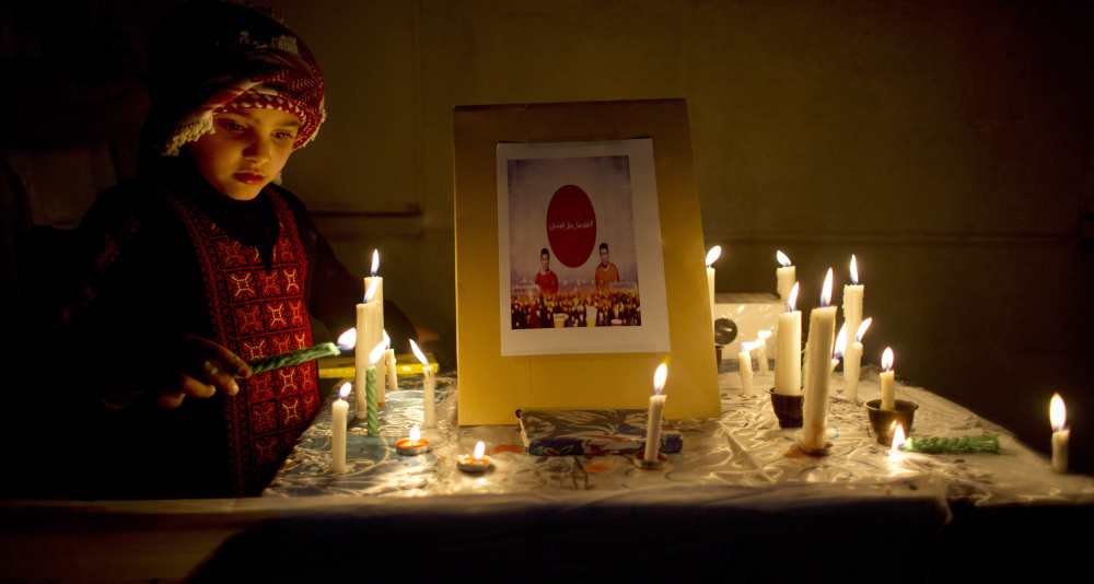 A Jordanian child lights a candle by a picture of two slain Japanese hostages Haruna Yukawa, right and Kenji Goto during a candle vigil in support of Japan, in front of the Japanese embassy, in Amman on Monday,