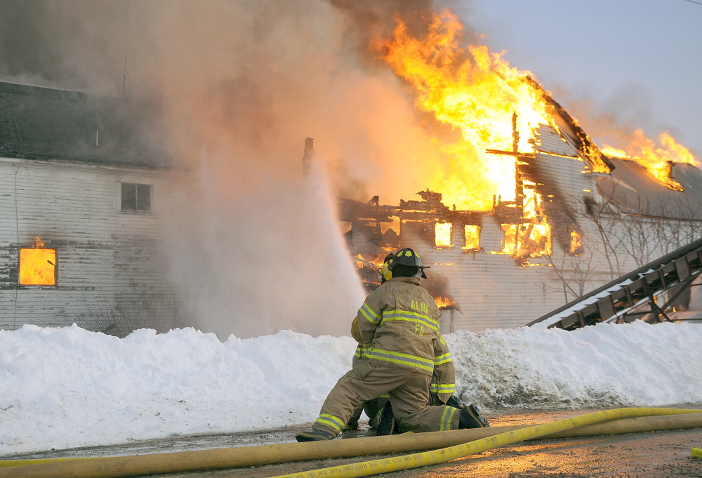 Firefighters attempt to prevent flames from the barn from spreading into the house on Tuesday at the Fenderson farm in Whitefield. The flames destroyed the dairy farm during the afternoon blaze.