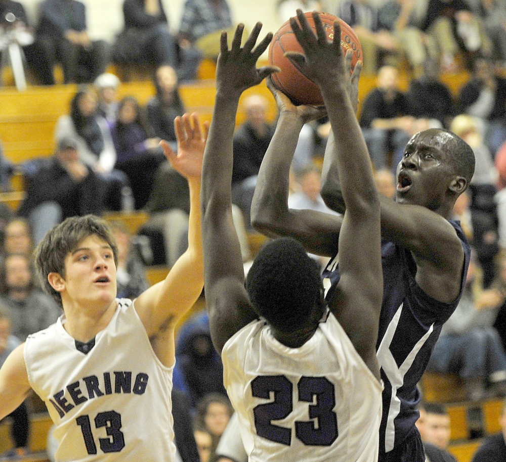 Stephen Alex takes a shot over Deering’s Max Chabot, left, and Garang Majok during Portland’s 66-44 win Thursday in Portland. Alex scored 27 points for the Bulldogs, who snapped a two-game losing streak.