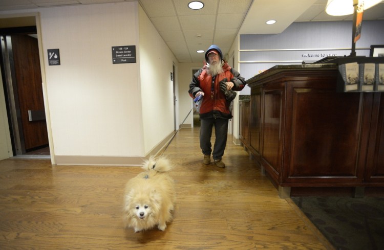 Richard Sweeney, who was displaced by the Jan. 29 fire at Centennial Place in Old Orchard Beach, walks through the lobby at the Hampton Inn in Saco with Easy Boy on Thursday. Some tenants worry that new short-term housing won’t accept pets.
