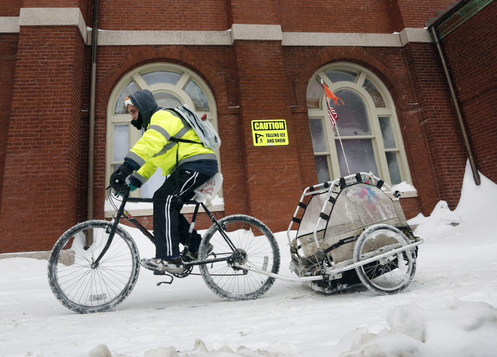 Gilbert Rosado of Portland rides past Sacred Heart Church on Mellen Street as the snow continues to fall on Sunday.