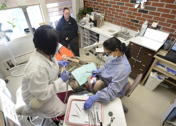 Alexzander Sprague, 14, is watched by his mother, Kelly Cousins of Buxton, as he gets a new filling from Dr. Vani Mallipeddi, right, and dental assistant Bich Ngoc Doan at Community Dental in Portland. Cousins, a mother of four, said she couldn’t find a dentist near Buxton who would accept MaineCare patients.