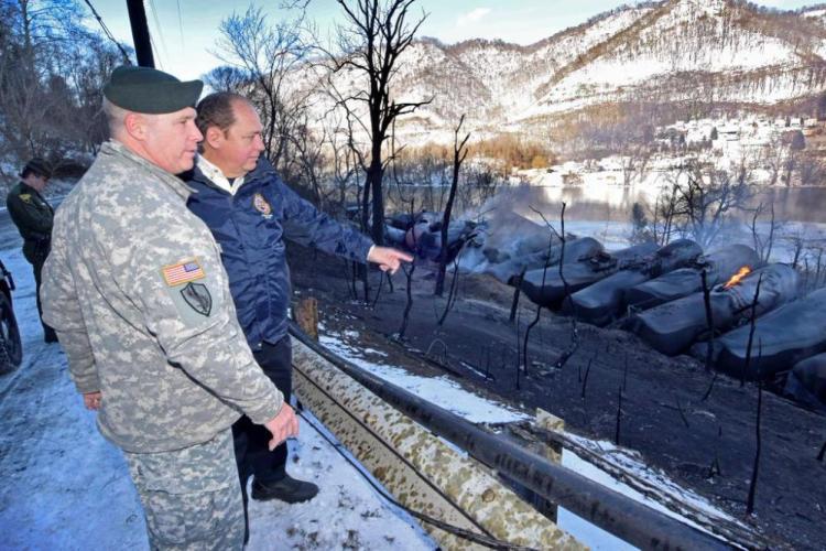 In this photo provided by the Office of the Governor of West Virginia, Gov. Earl Ray Tomblin, second from left, and Gen. James Hoyer stand near derailed train cars near Mount Carbon, W.Va., Tuesday.