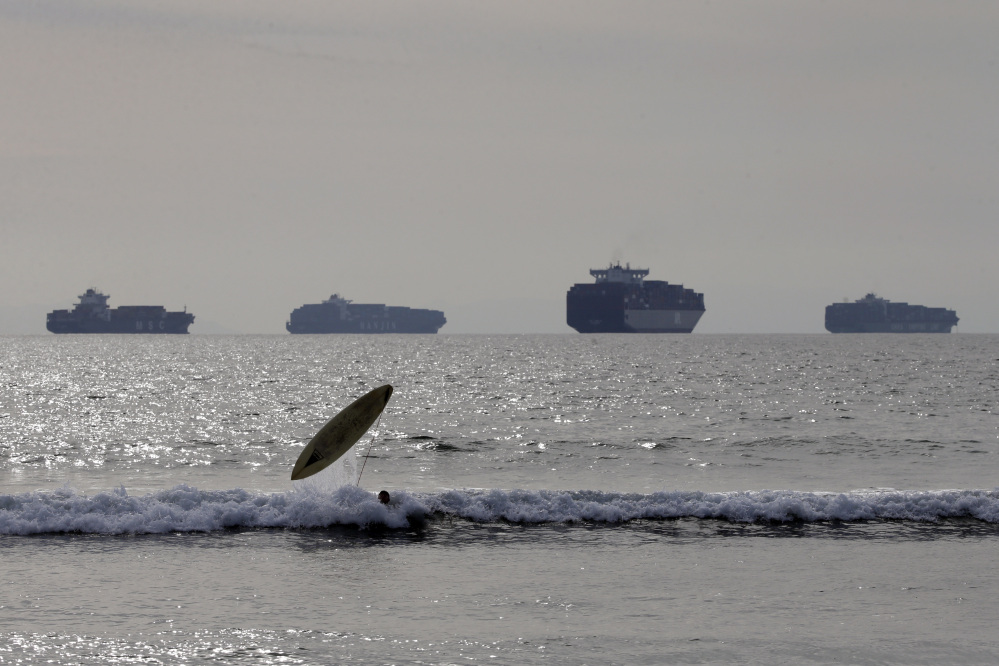 Jake Ferguson loses his surfboard while riding a wave Friday in Sunset Beach, Calif., as loaded cargo ships are anchored outside the Ports of Long Beach and Los Angeles.