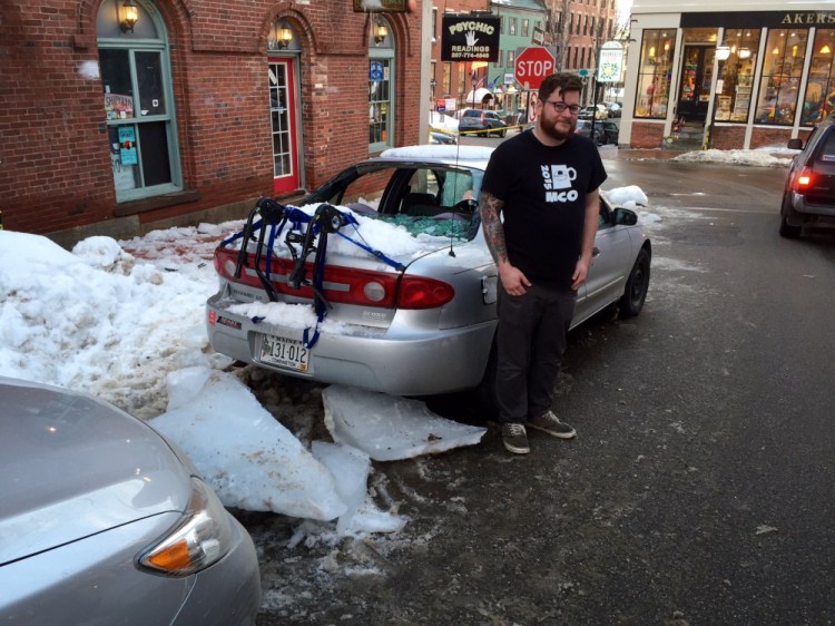 Adam Sousa stands by his car after it was hit by ice that fell off a building on Exchange Street. Dennis Hoey/Staff Writer