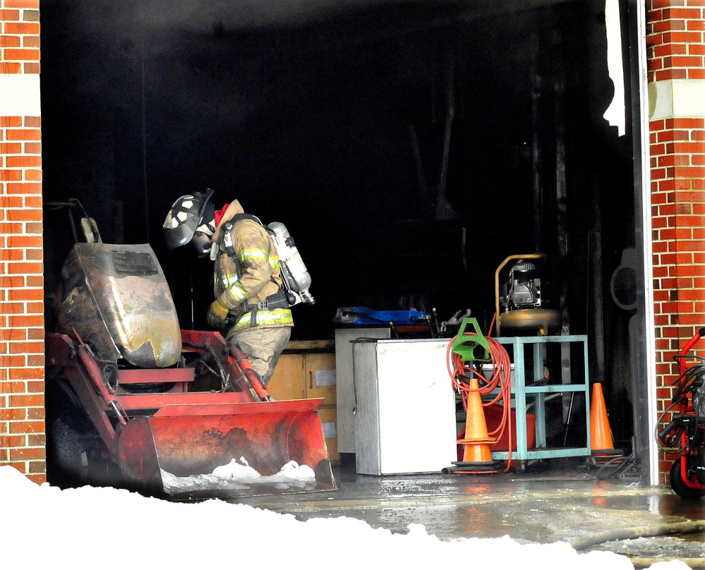 A firefighter looks over a small tractor that caught fire inside a garage attached to the Vassalboro Community School on Sunday. The fire did substantial damage to the garage and equipment, and firefighters from Vassalboro and Winslow had to use fans to ventilate other parts of the school fouled by black smoke.