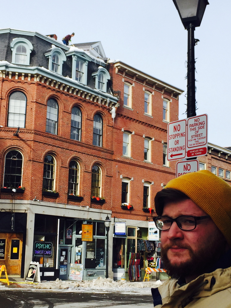 Adam Sousa stands in front of the building at the corner of Exchange and Fore streets, where large pieces of ice fell on his car Sunday. He has since received broad support from the community to get back on the road.