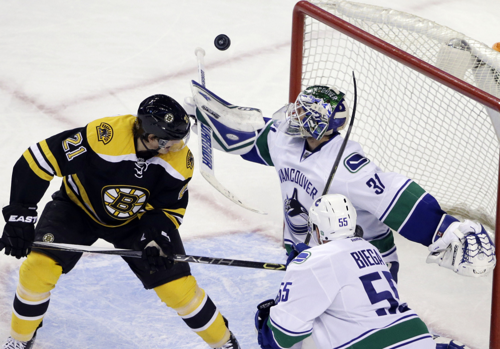 Vancouver Canucks goalie Eddie Lack keeps an eye on the rebounding puck as Bruins left wing Loui Eriksson watches along with Canucks defenseman Alex Biega during the third period of Tuesday night’s game in Boston. The Bruins lost, and now have just one win in their last nine games.