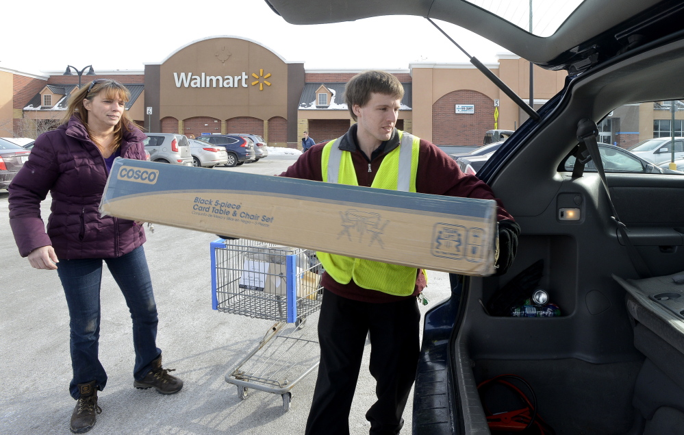 Thomas Bailey, right, a Wal-Mart employee at the company’s Scarborough store, assists customer Theresa Graham of Windham with a purchase Tuesday. Bailey, who trains fellow Wal-Mart workers, says it has been fun to share the news of the pay increase with new hires.