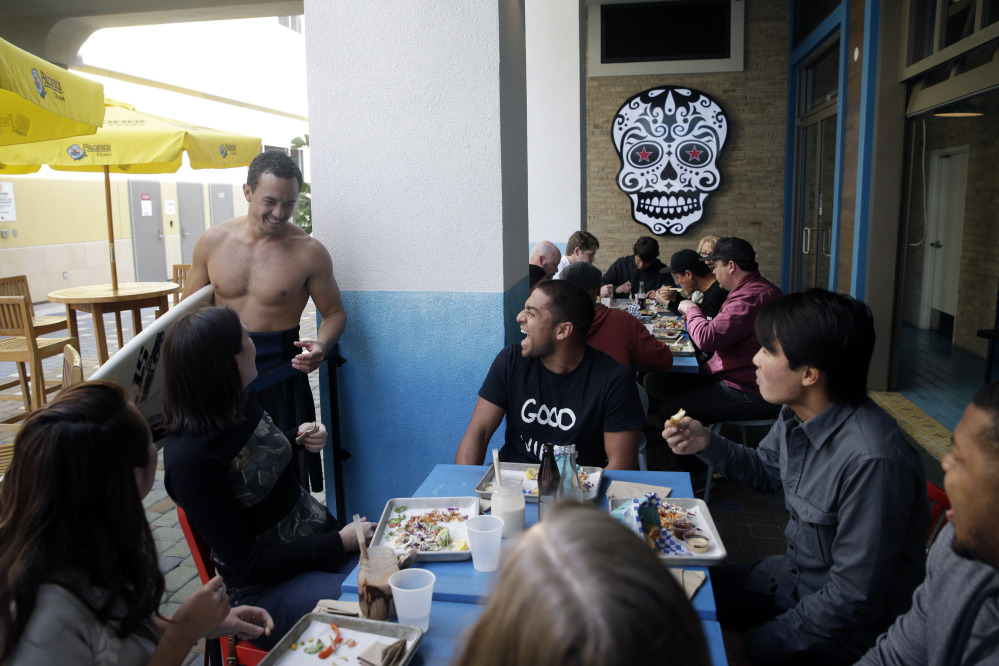 Nathan Seymour, top left, with a surfboard, chats with his friends at U.S. Taco Co., which is owned by Taco Bell, in Huntington Beach, Calif. The Associated Press