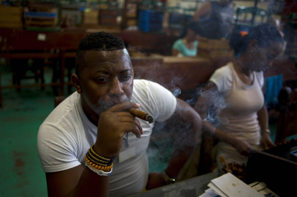Quality control employee Manuel Lamoth, 30, smokes a cigar at the Corona cigar factory in Havana, Cuba, Thursday. Cuban cigar makers are happy with new U.S. rules that let more Americans travel to the island and legally bring back as much as $100 worth of cigars for the first time in decades. Officials said during this week's annual cigar festival that this year alone, they expect to double sales of hand-rolled "habanos" on the island. The Associated Press