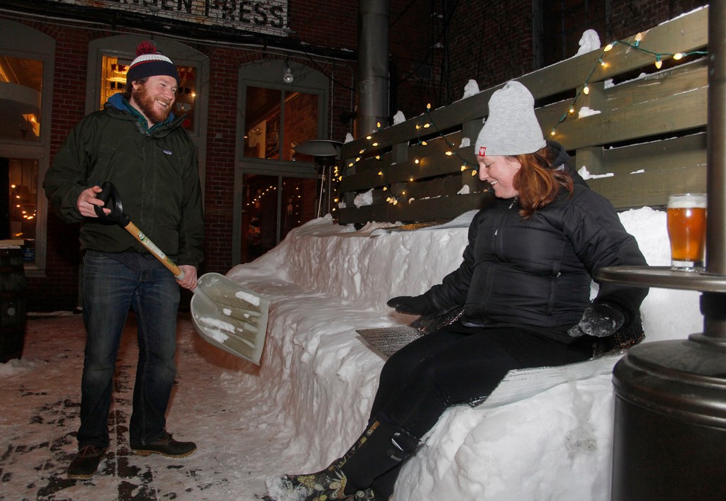 Trevor Fischer, a bartender at The Thirsty Pig, watches as Margaret Keilty of South Portland tries out the seating he made out of snow where patrons were invited to watch the 
Super Bowl projected on a neighboring brick wall  Sunday. Jill Brady/Staff Photographer