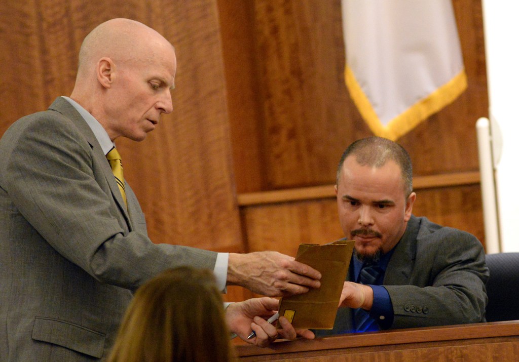 Assistant District Attorney William McCauley, left, shows former Massachusetts State Police officer Edward Reece an evidence bag containing shell casings Reece marked as he testifies during the murder trial of Aaron Hernandez. The Associated Press