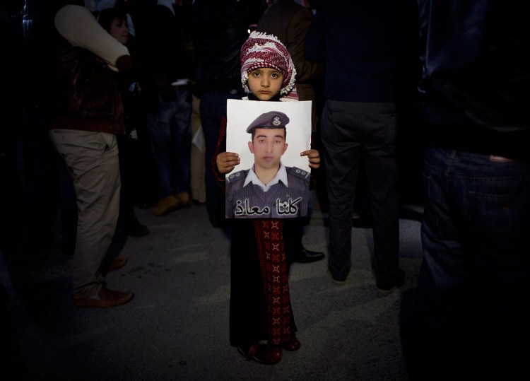 A Jordanian child holds a poster with a picture of Jordanian pilot Lt. Muath al-Kaseasbeh, with a message in Arabic that reads, "We are all Muath." 