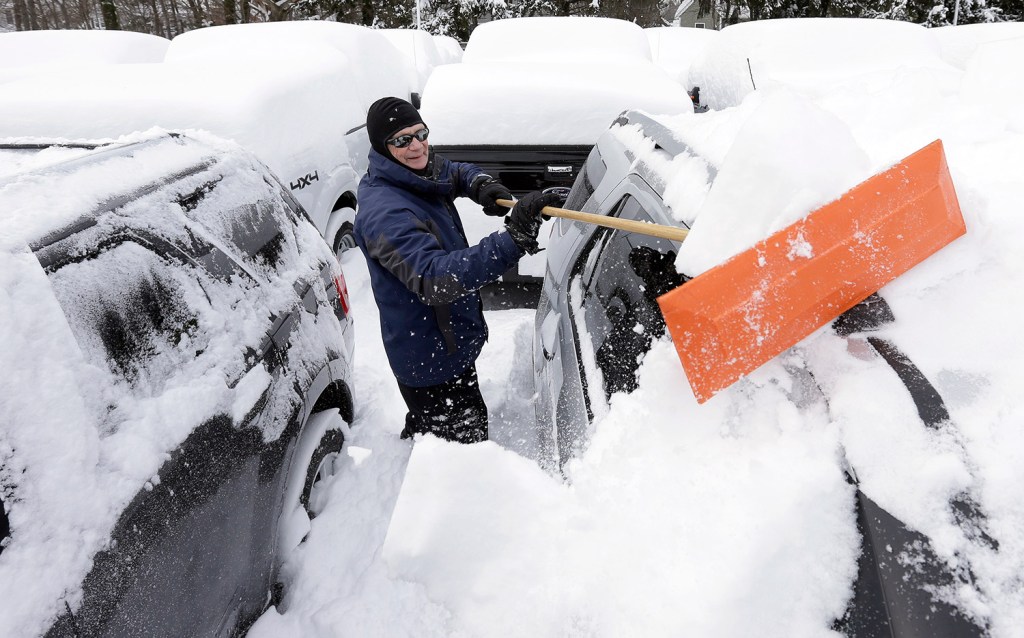 Lealand Welsh, of Wrentham, Mass., removes snow from cars and trucks at a Ford dealership in Norwood, Mass. 