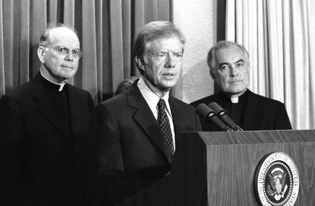 President Jimmy Carter announces a pledge of $67 million in humanitarian relief for Cambodia at the White House on Oct. 24, 1979. Standing at right is The Rev.  Theodore M. Hesburgh, president of Notre Dame University. At left is Cardinal Terence Cooke. The Associated Press