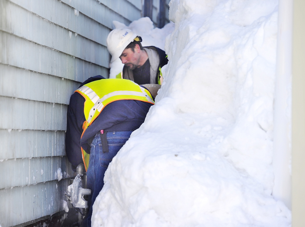 Workers from Unitil Corp. gas company repair the gas meter after clearing the snow from it at an apartment building on Congress Street on Portland’s Munjoy Hill on Friday.
