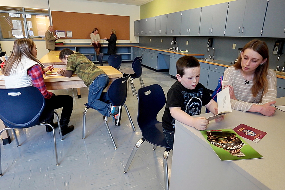 Megan Brown, 18, right, a volunteer reading mentor in the Teen Trendsetters program, helps Jacob Rice, 6, read a book at Buxton Center Elementary School. “It’s nice when they catch onto something,” Brown said. Their success “makes you really feel good.”
