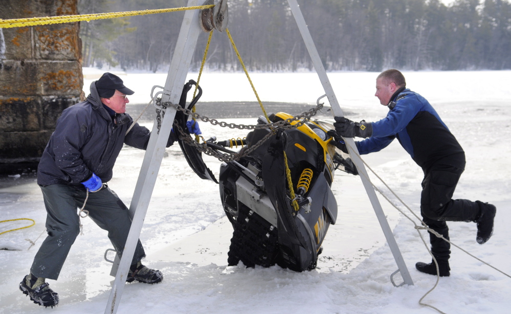 Matt Sinclair, right, and his father, David, secure a snowmobile they hoisted from under the ice on Maranacook Lake in Winthrop on Sunday.